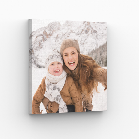 A wrapped canvas print of a mother and child enjoying the snow, hanging on a white wall.