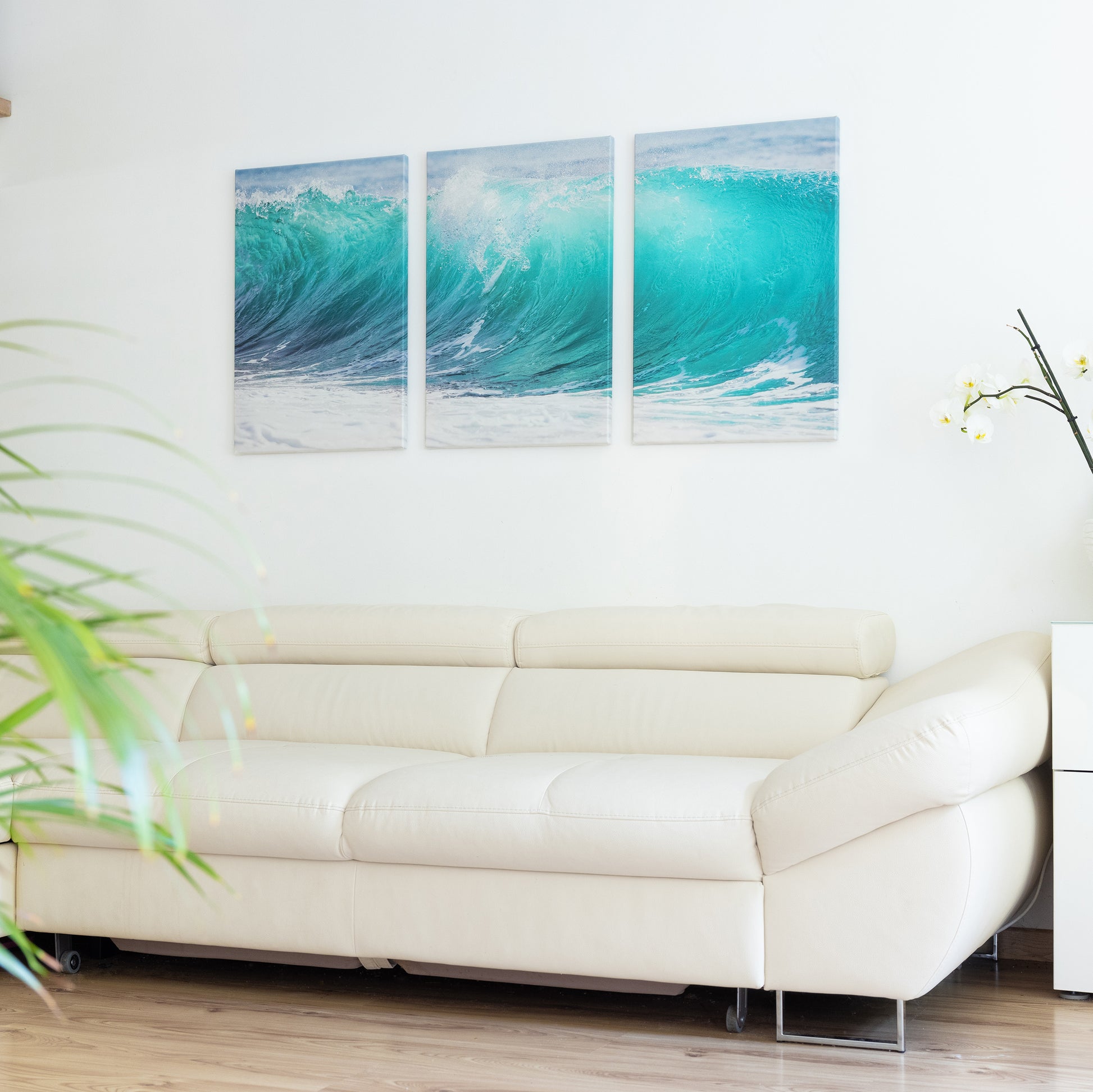 Three-panel artwork of ocean waves above a white sofa in a living room.