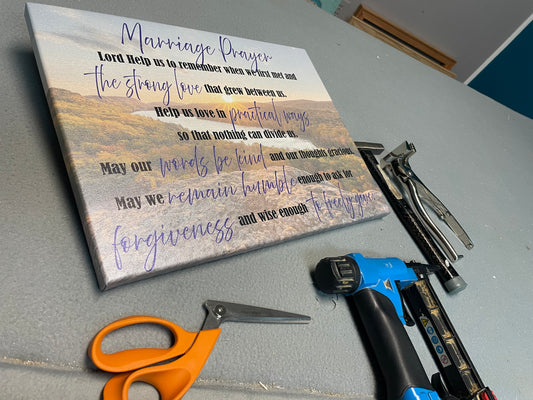 Decorative canvas with text on a table with tools like scissors and a staple gun.