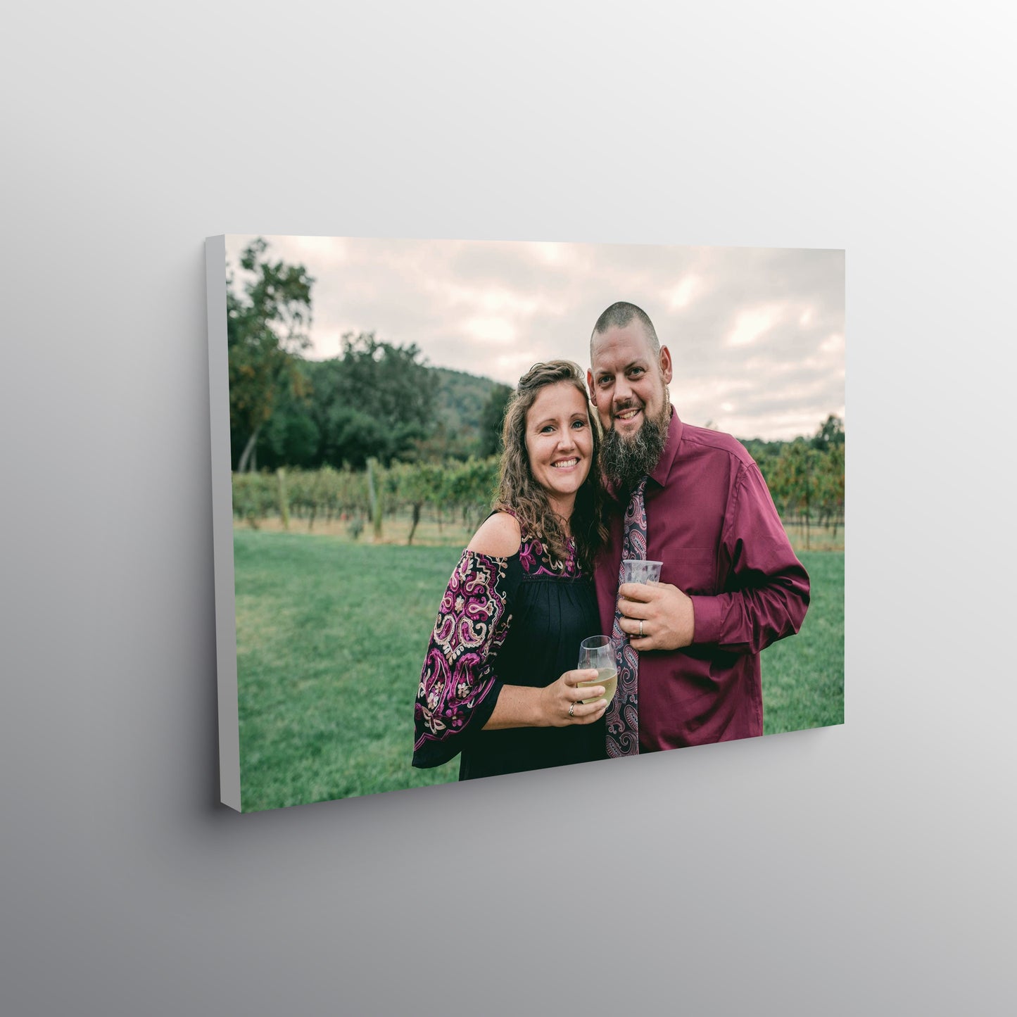A stretched canvas print of a couple in a vineyard, hanging on a gray wall.